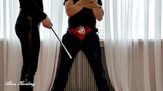 Alice tied up the guy and hits him in the penis and groin with a rod and a leg