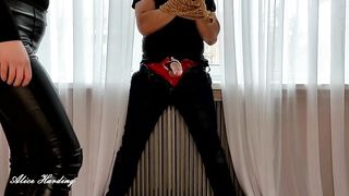 Alice tied up the guy and hits him in the penis and groin with a rod and a leg